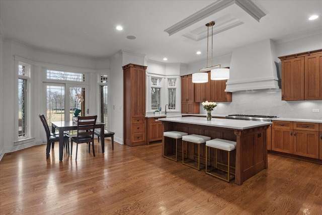 kitchen with light countertops, a kitchen island, premium range hood, dark wood-style floors, and brown cabinetry