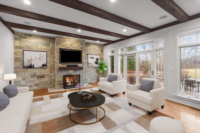 living area with a fireplace, visible vents, light wood-style floors, and beam ceiling