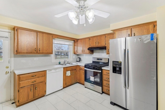 kitchen with appliances with stainless steel finishes, under cabinet range hood, light countertops, a sink, and brown cabinets