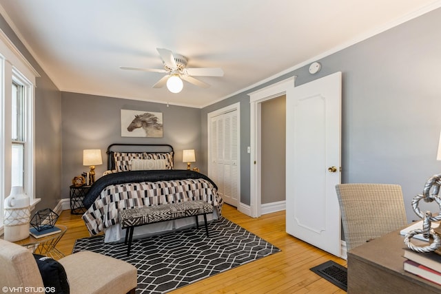 bedroom featuring light wood-type flooring, baseboards, crown molding, ceiling fan, and a closet