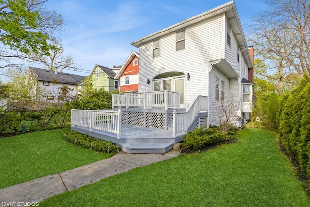 back of property with a chimney, a wooden deck, and a yard