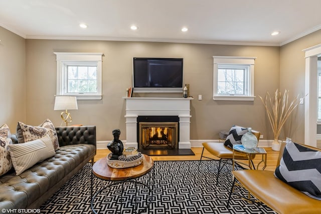 living area featuring wood finished floors, recessed lighting, a glass covered fireplace, ornamental molding, and baseboards