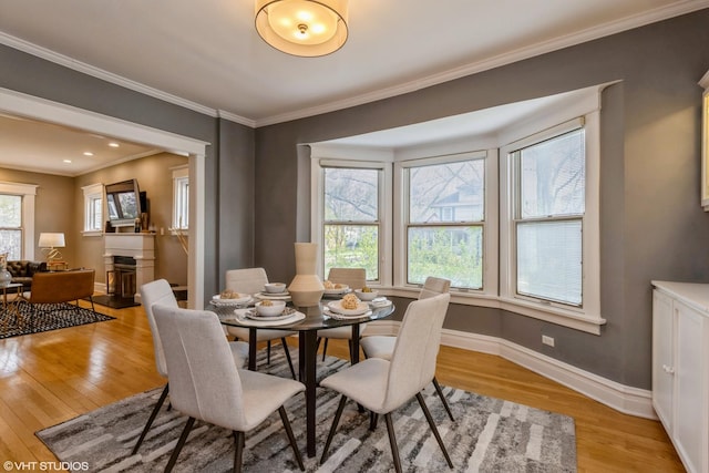 dining room featuring light wood-style floors, baseboards, ornamental molding, and a fireplace