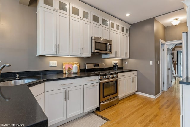 kitchen featuring appliances with stainless steel finishes, a sink, light wood-style floors, white cabinetry, and recessed lighting