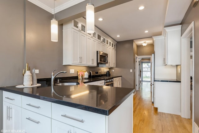 kitchen featuring stainless steel appliances, a sink, a peninsula, white cabinetry, and crown molding