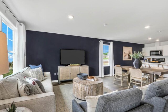 living area featuring baseboards, wood finished floors, recessed lighting, and an accent wall
