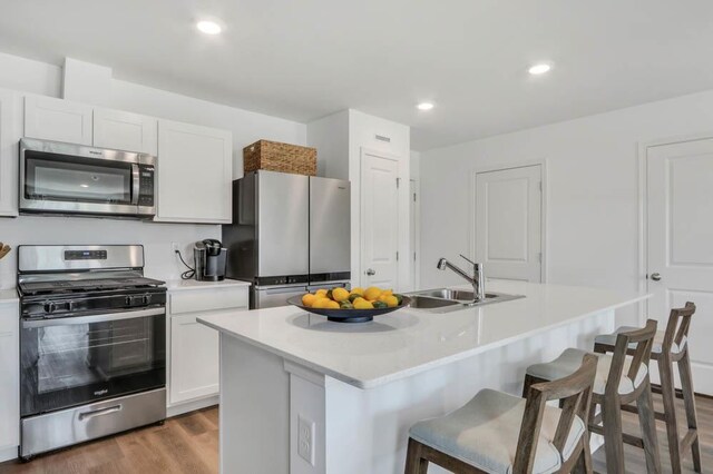 kitchen featuring white cabinets, light countertops, a kitchen bar, appliances with stainless steel finishes, and a sink