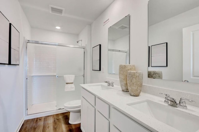 bathroom featuring toilet, a sink, a stall shower, and visible vents