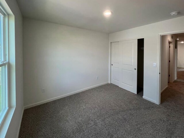 unfurnished bedroom with baseboards, dark carpet, and a closet