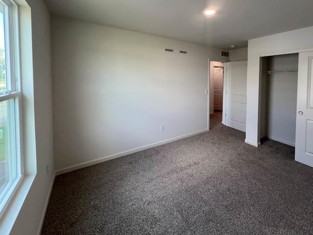 unfurnished bedroom with a closet, baseboards, dark colored carpet, and visible vents