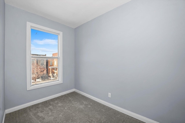 spare room featuring baseboards and dark colored carpet