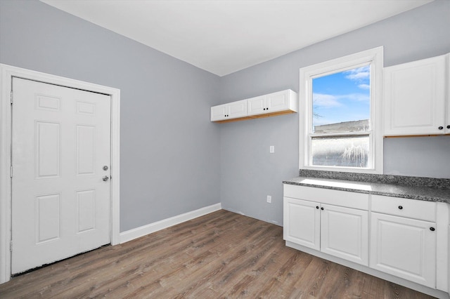 kitchen with white cabinetry, dark countertops, baseboards, and wood finished floors