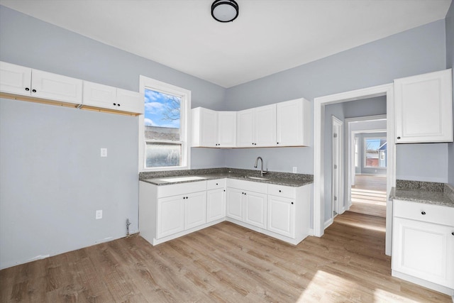kitchen with white cabinets, light wood-style floors, a sink, and dark stone counters