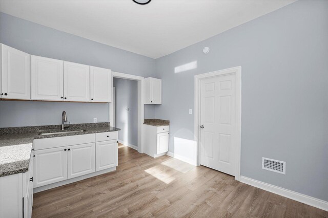 kitchen with a sink, light wood-type flooring, baseboards, visible vents, and white cabinets