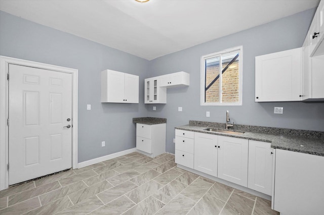 kitchen featuring white cabinets, a sink, dark countertops, and baseboards