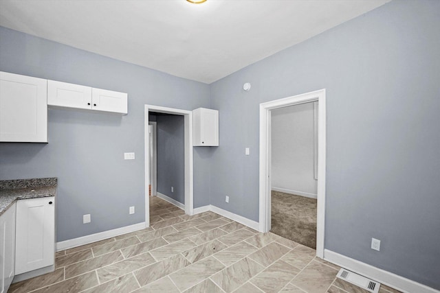 kitchen with white cabinetry, dark stone counters, baseboards, and visible vents