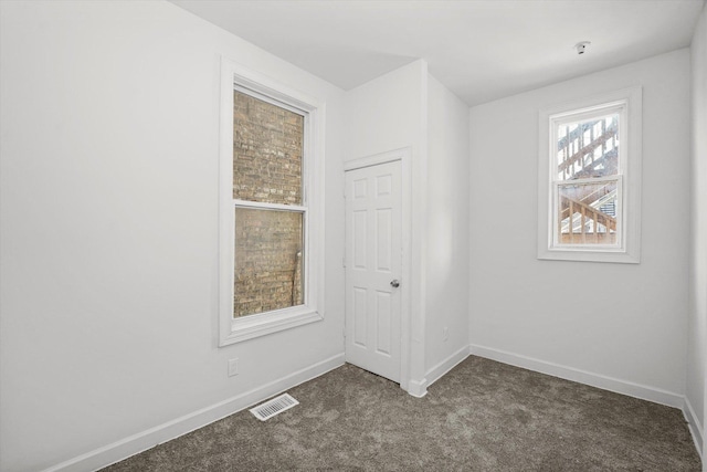 empty room with baseboards, visible vents, and dark carpet