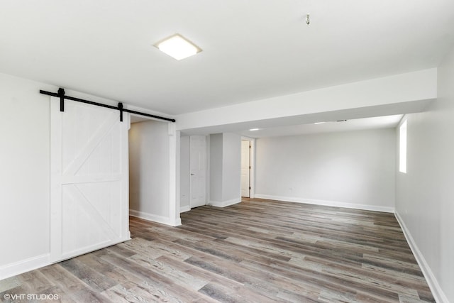 below grade area with baseboards, a barn door, and wood finished floors