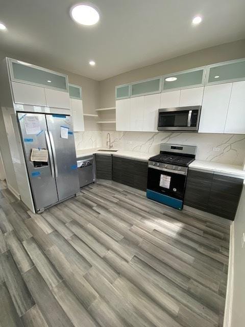kitchen featuring light wood-type flooring, appliances with stainless steel finishes, a sink, and open shelves