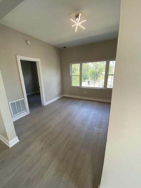 empty room with a chandelier, visible vents, baseboards, and wood finished floors
