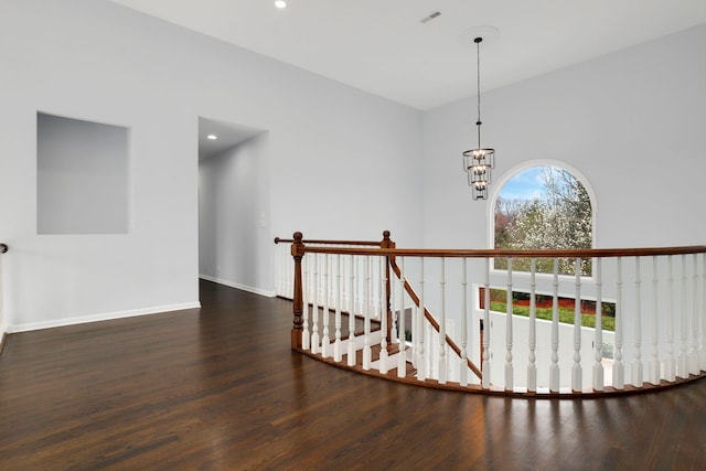 hallway with an inviting chandelier, wood finished floors, visible vents, an upstairs landing, and baseboards