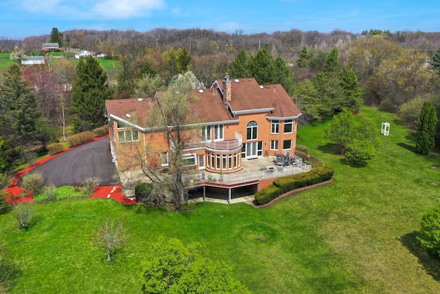 back of property featuring a forest view, a balcony, a lawn, a chimney, and a patio