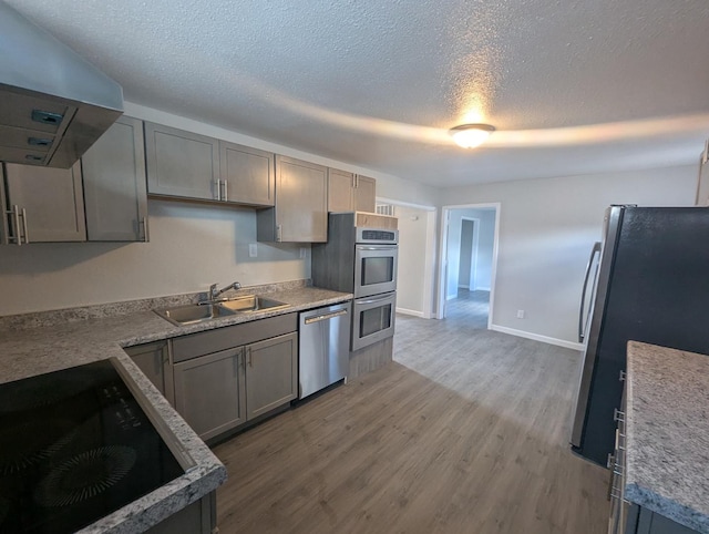 kitchen with a sink, range hood, wood finished floors, a textured ceiling, and stainless steel appliances