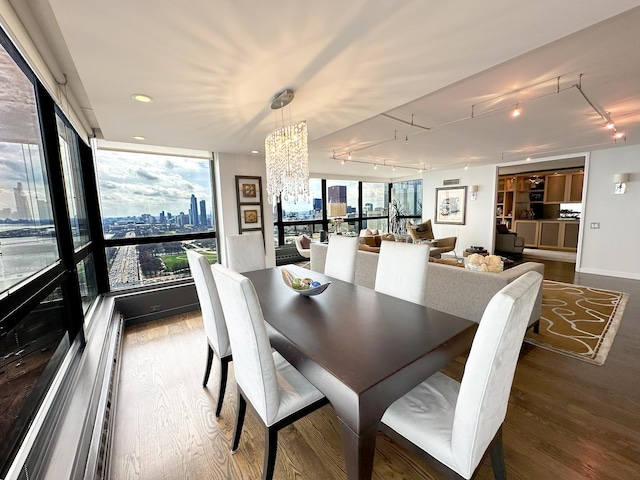 dining area with rail lighting, wood finished floors, a chandelier, expansive windows, and a view of city