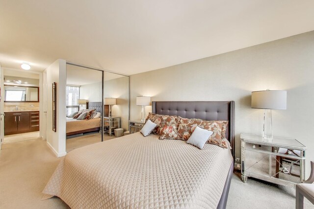 bedroom featuring light colored carpet, a closet, and ensuite bath