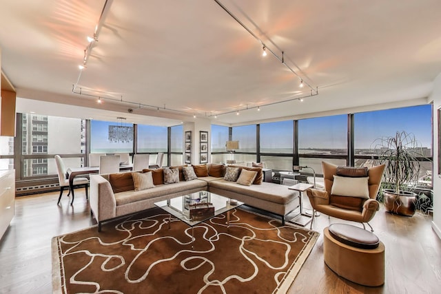 living room with rail lighting, wood finished floors, healthy amount of natural light, a water view, and a wall of windows