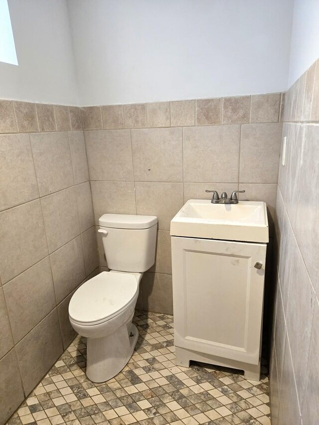 half bath with vanity, tile walls, and toilet