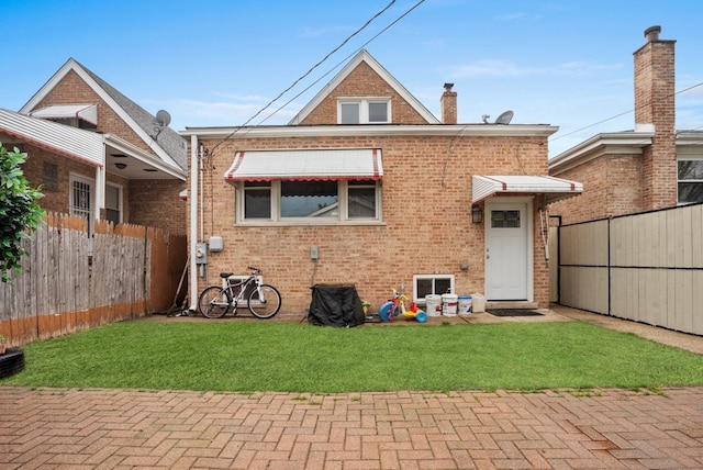 back of house featuring fence, a lawn, and brick siding
