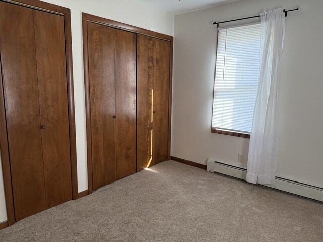 unfurnished bedroom with two closets, carpet flooring, baseboard heating, and baseboards