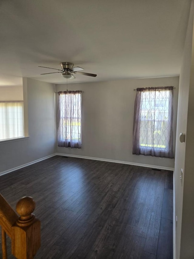spare room featuring dark wood-type flooring, ceiling fan, baseboards, and a healthy amount of sunlight