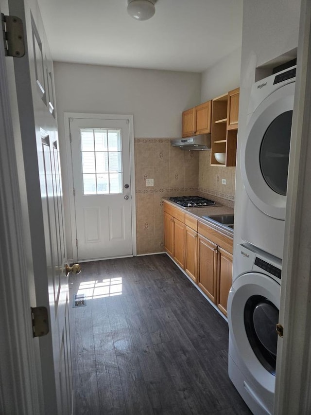 washroom with dark wood-type flooring, stacked washing maching and dryer, and laundry area