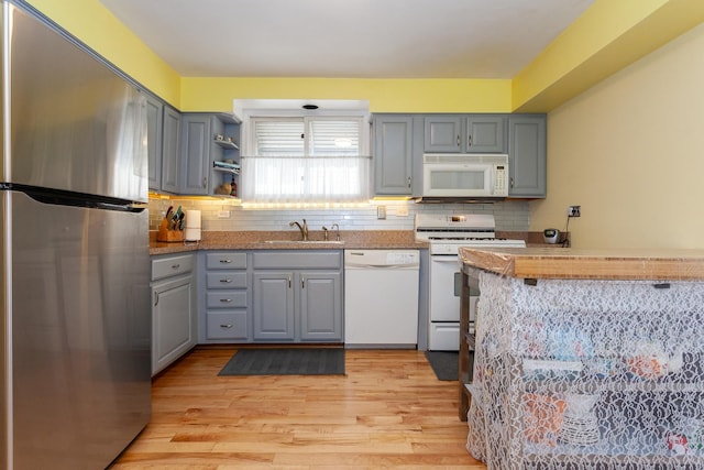 kitchen featuring gray cabinets, a sink, light wood-style flooring, and white appliances