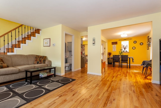 living room with baseboards, light wood-style floors, and stairs