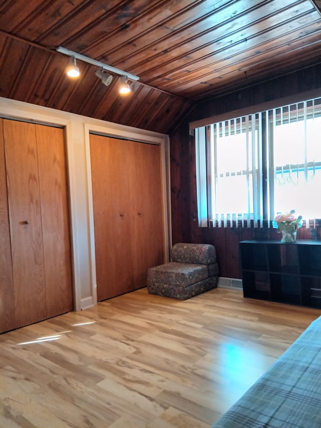 unfurnished bedroom with two closets, wood walls, vaulted ceiling, wooden ceiling, and wood finished floors