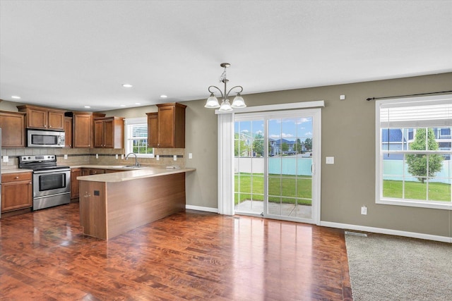 kitchen with appliances with stainless steel finishes, a peninsula, a chandelier, light countertops, and tasteful backsplash