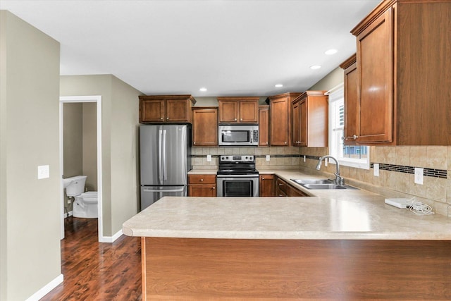 kitchen featuring stainless steel appliances, a sink, backsplash, a peninsula, and recessed lighting
