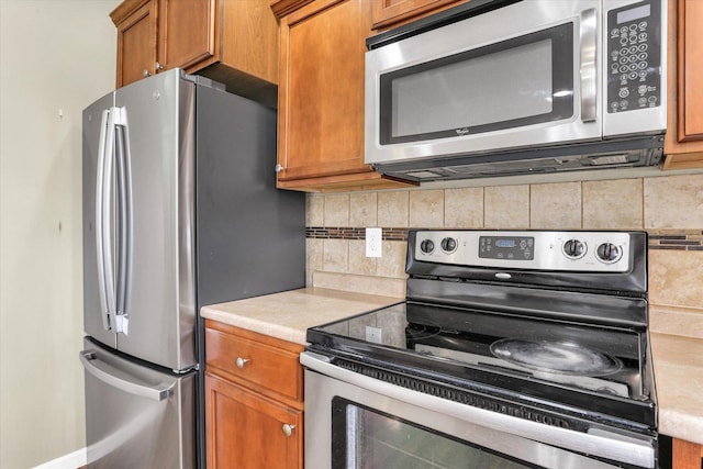 kitchen with stainless steel appliances, tasteful backsplash, light countertops, and brown cabinetry