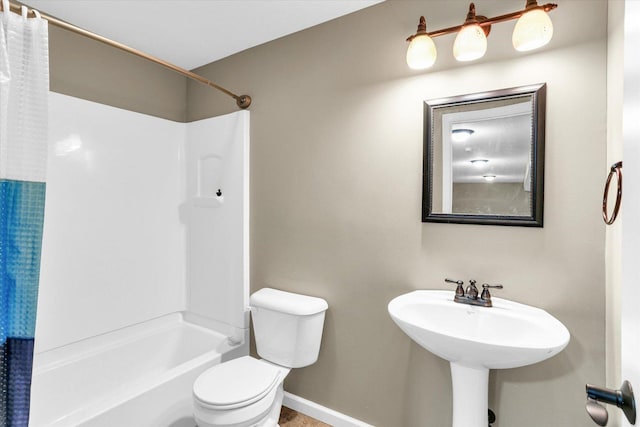 full bath with toilet, baseboards, shower / bath combo, and a sink