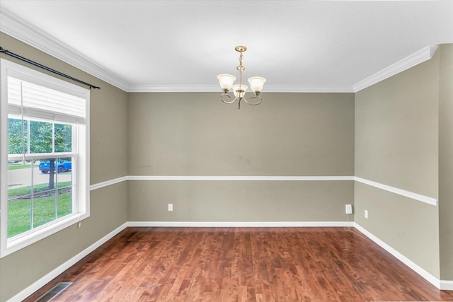 spare room featuring a chandelier, healthy amount of natural light, wood finished floors, baseboards, and crown molding