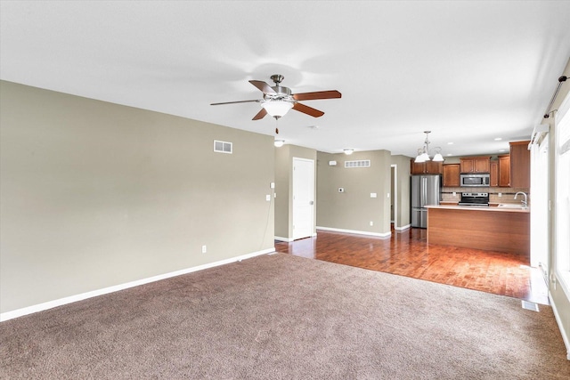 unfurnished living room with dark colored carpet, a chandelier, baseboards, a ceiling fan, and a sink