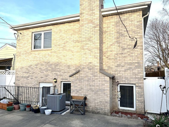 rear view of property with central AC unit, fence, a chimney, brick siding, and a patio area