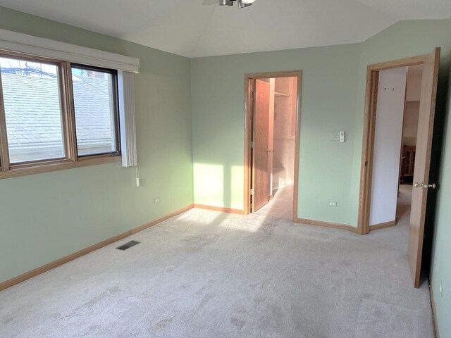 unfurnished bedroom with baseboards, lofted ceiling, visible vents, and light colored carpet