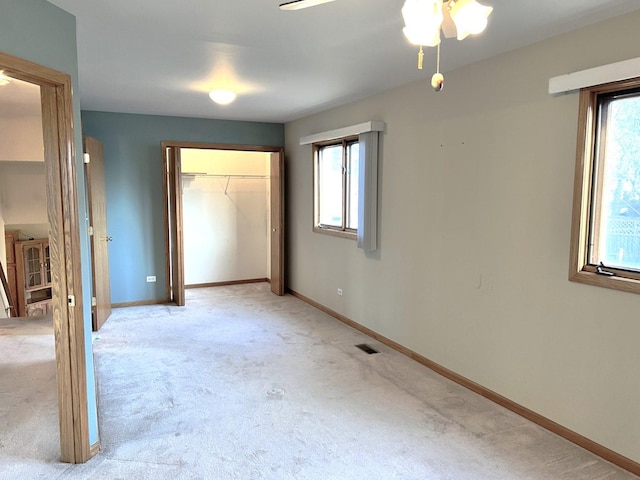 unfurnished bedroom featuring baseboards, visible vents, multiple windows, and light carpet