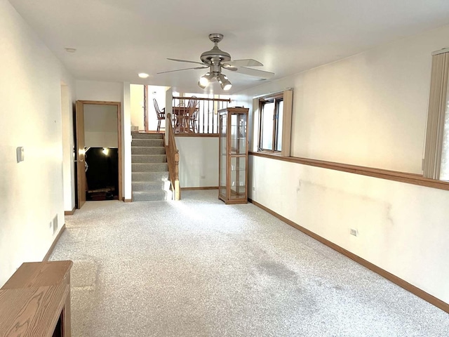 carpeted empty room with baseboards, ceiling fan, visible vents, and stairway
