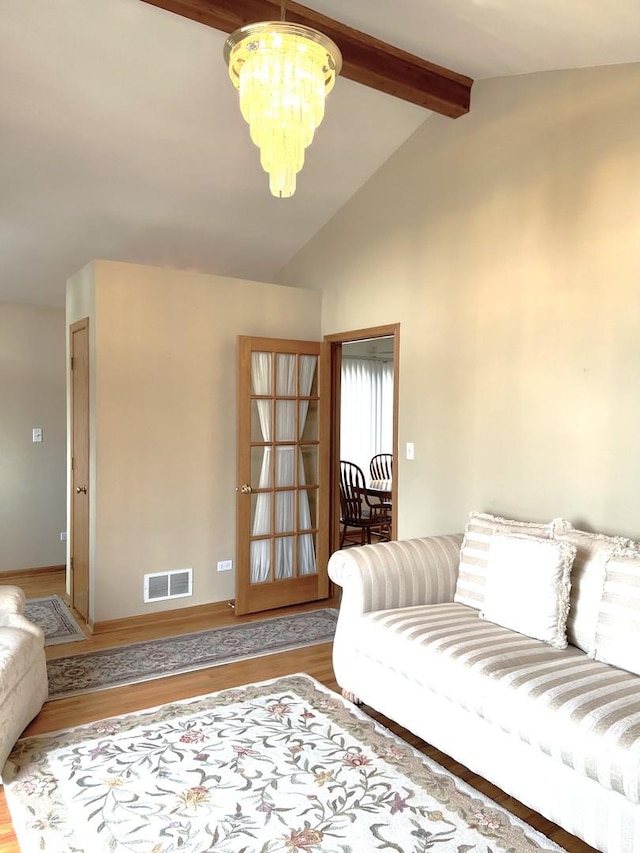 living room featuring lofted ceiling with beams, wood finished floors, baseboards, visible vents, and an inviting chandelier