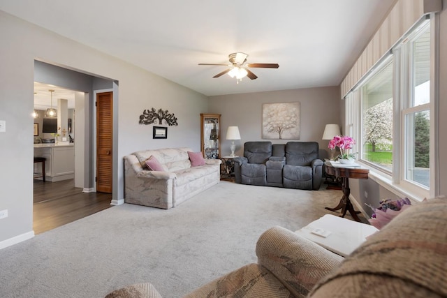 carpeted living room with baseboards and a ceiling fan
